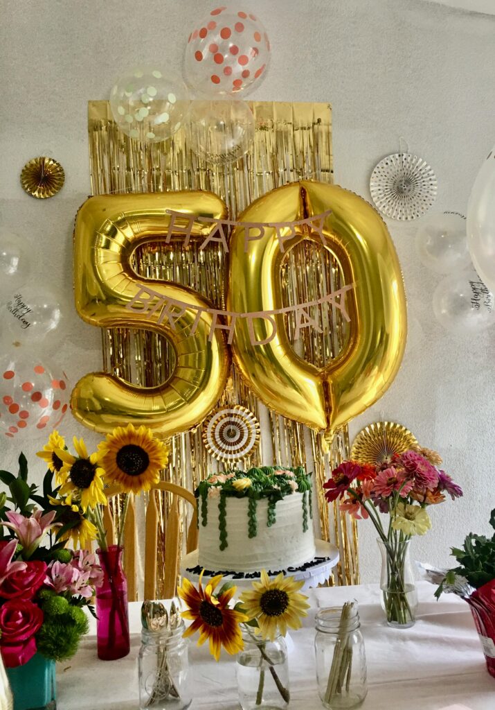 Luxurious 50th birthday party scene with golden balloons and floral cake.